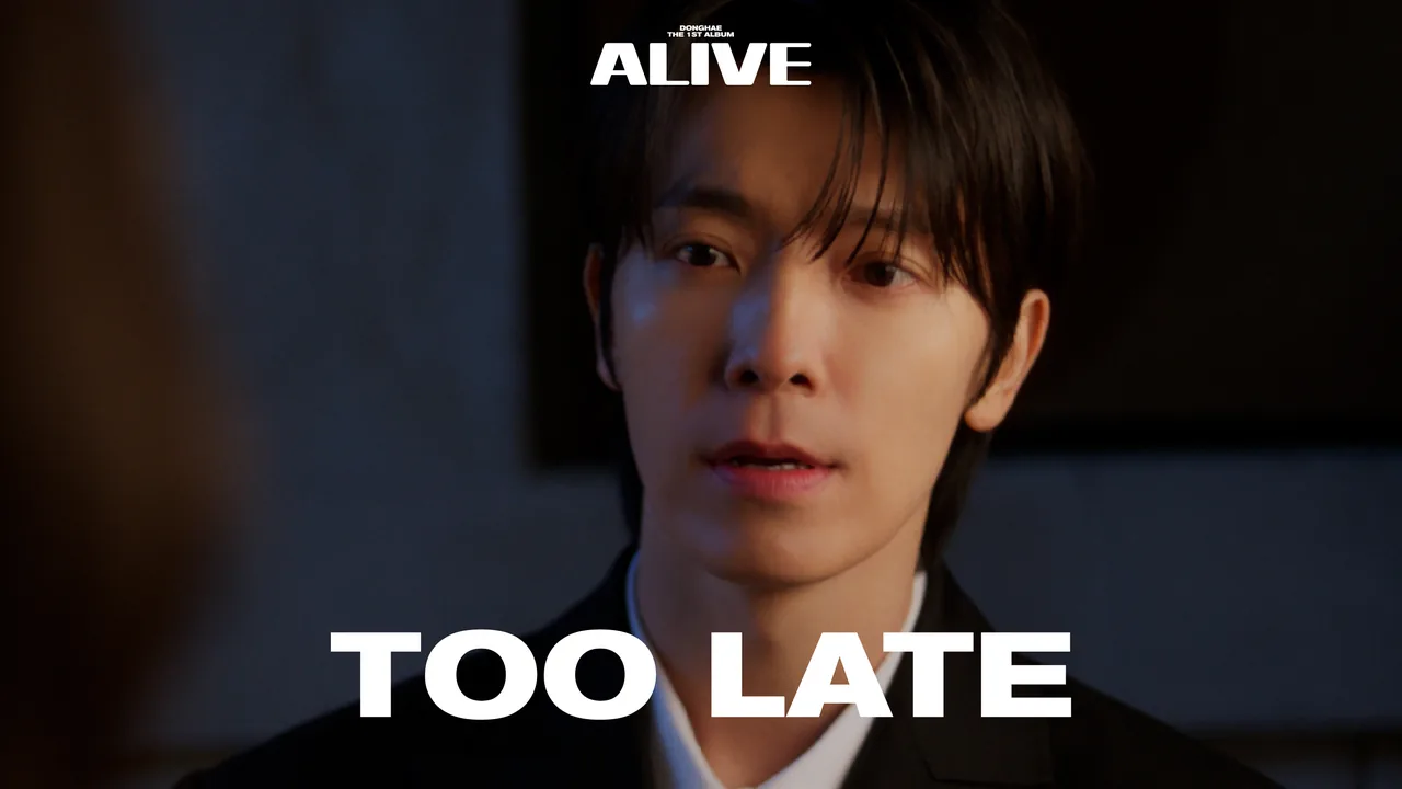 Still from the Too Late music video — DONGHAE in low blue light, suited, looking past the camera